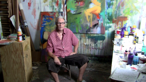 that famous award winning artist andy morris sitting in his studio big dirty paint brush in hand huge abstract painting behind him in bold colors
